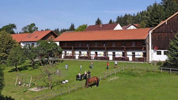Um estábulo com cavalos e pessoas, cercado por uma área vedada e edifícios com telhados vermelhos.