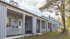 A row of single-story buildings with a porch, wooden railings, and a grassy area in front.