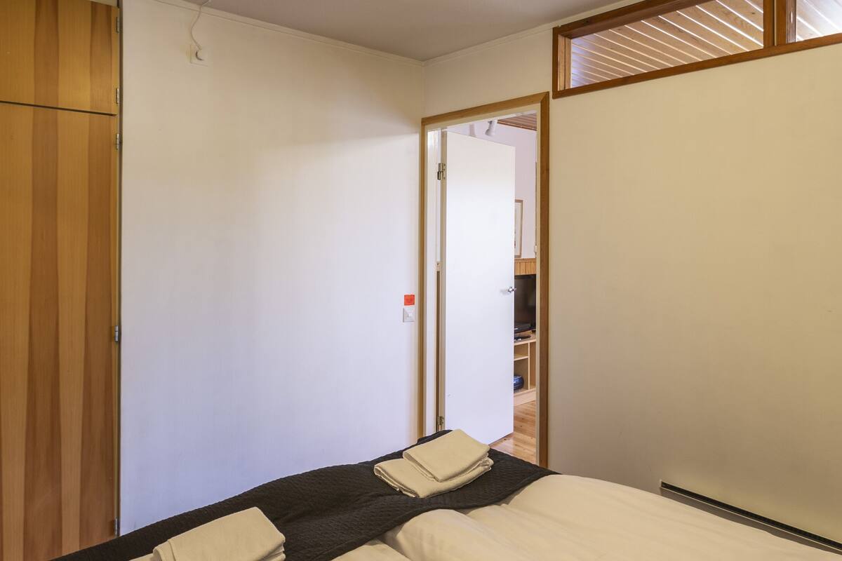 A hotel room with two beds, a wooden wardrobe, a white ceiling, and a door leading to another room.