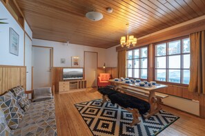 Ein gemütlicher Raum mit Holzböden, einer Couch, einer Bank, einem Esstisch mit Stühlen und einem großen Fenster mit Vorhängen.
