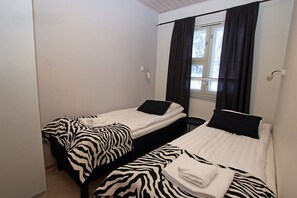 Ein Zimmer mit zwei Einzelbetten, Bettwäsche mit Zebra-Muster, einem Fenster mit dunklen Vorhängen und einer weißen Wand.