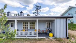 A single-story house with a porch, a small outdoor seating area with chairs and a table, and a covered outdoor area with a grill.