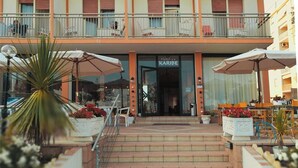 Een hotelentree met een bord waarop "Hotel Karibe" staat, zitplaatsen buiten met parasols, en een trap die naar de entree leidt.