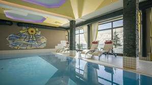 Piscina com espreguiçadeiras, mural de sol e amplas janelas com vista para montanhas cobertas de neve.
