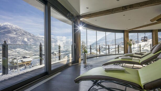Uma sala de estar moderna com janelas amplas que oferecem vista para as montanhas, guarda-corpo de vidro e teto de madeira.