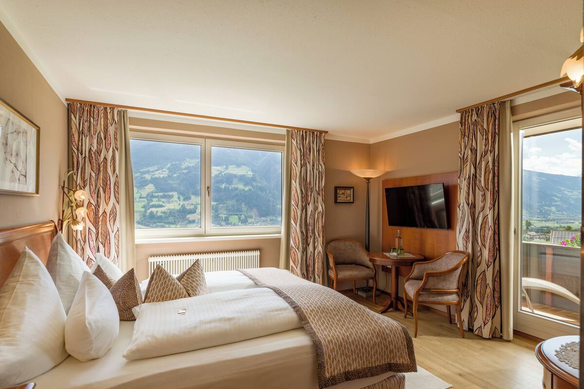 A hotel room with a large bed, a desk, a chair, and a TV.