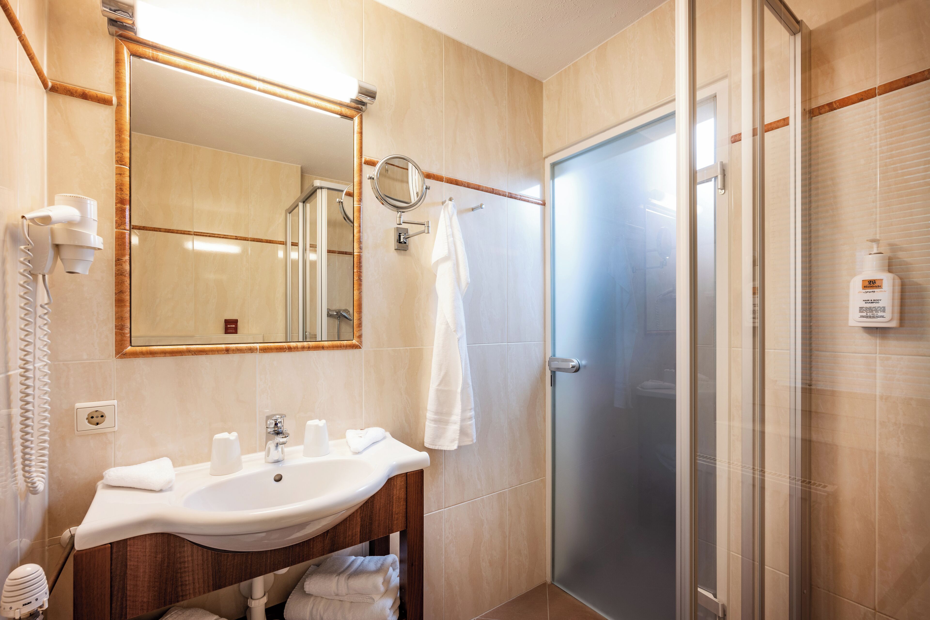 Ein Hotelbad mit Waschbecken, Spiegel, Handtuchhalter und Duschbereich.