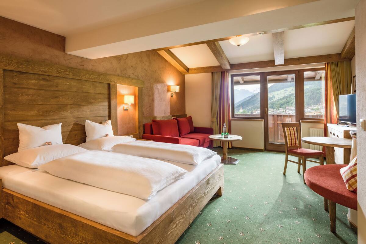 A hotel room with a large bed, a red sofa, a small table, and a view of mountains.