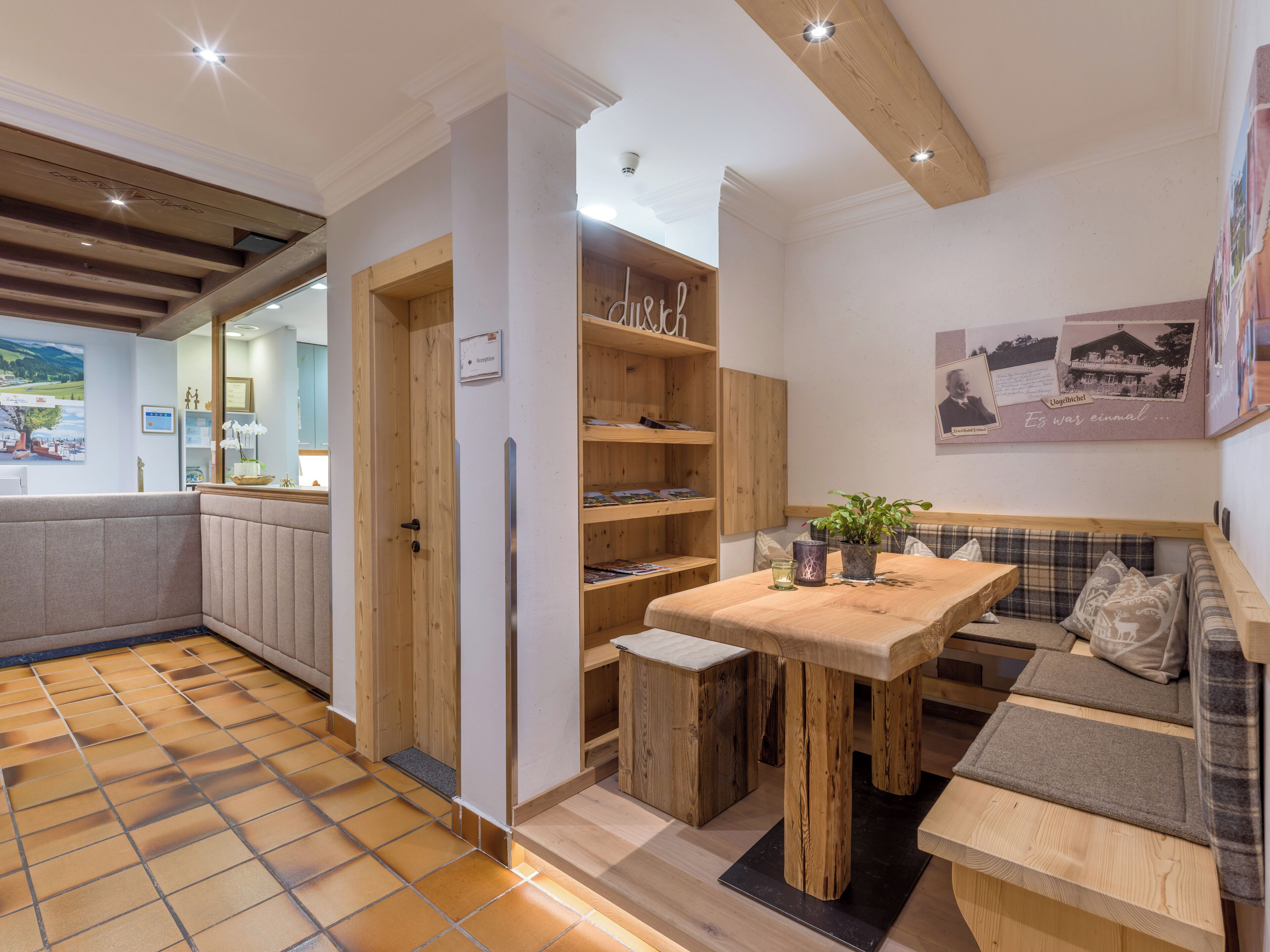 Une cuisine chaleureuse avec des meubles en bois, une table à manger et un coin salon comprenant un banc et des coussins.