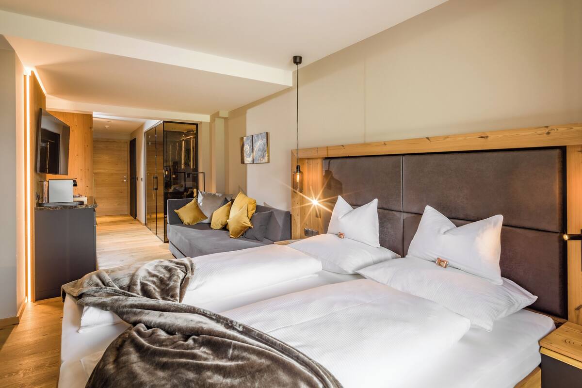 A modern hotel room with a large bed, a sofa, and a wooden headboard.