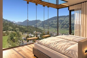 A bedroom with a large bed, wooden flooring, and a view of a mountainous landscape. - Hotel Waldfriede (Fuegenberg)