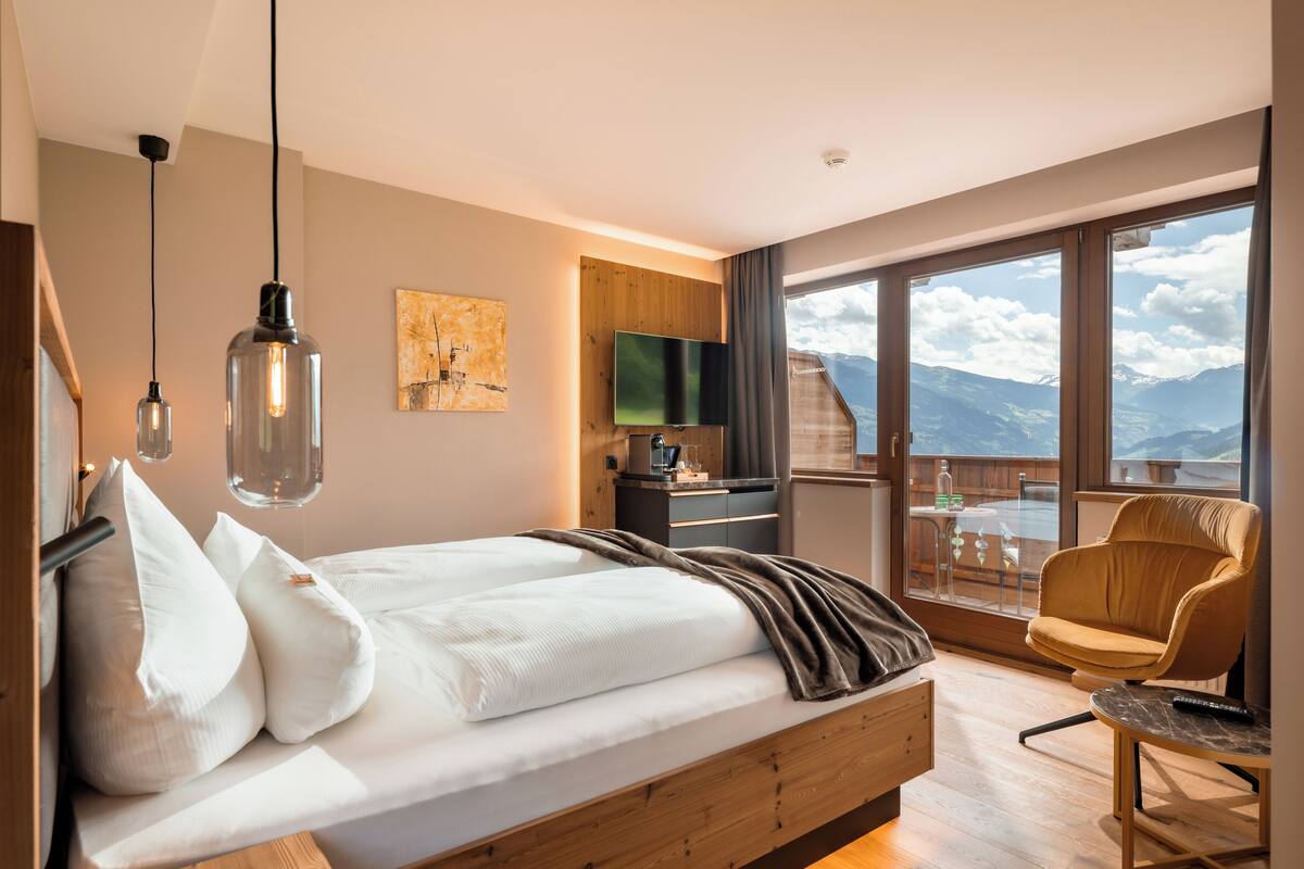 A modern bedroom with a wooden bed, a desk, and a balcony with a view of mountains.