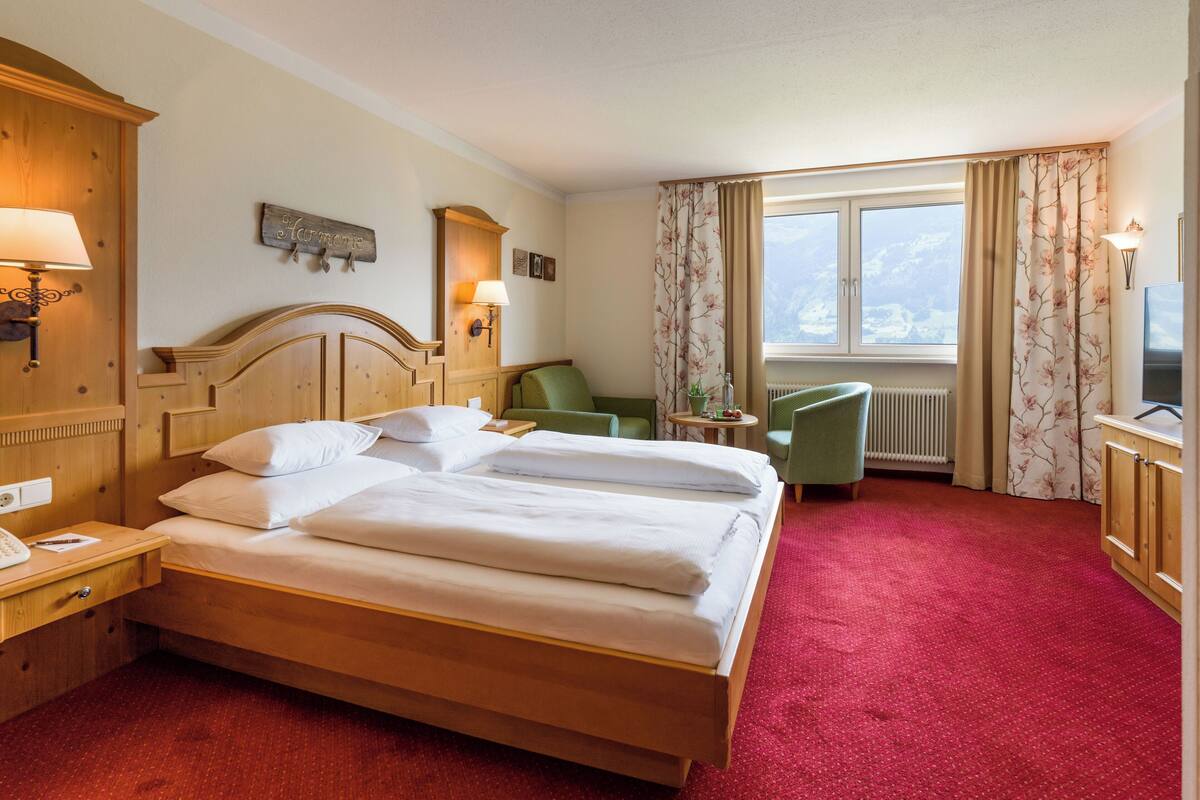 A hotel room with a large bed, a desk with a lamp, a chair, and a view of a snowy landscape through the window.