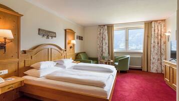 A hotel room with a large bed, a desk with a lamp, a chair, and a view of a snowy landscape through the window.