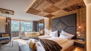 Quarto de hotel moderno com teto de madeira, uma cama grande com peseira, um sofá, uma mesa de centro e vista para o exterior.