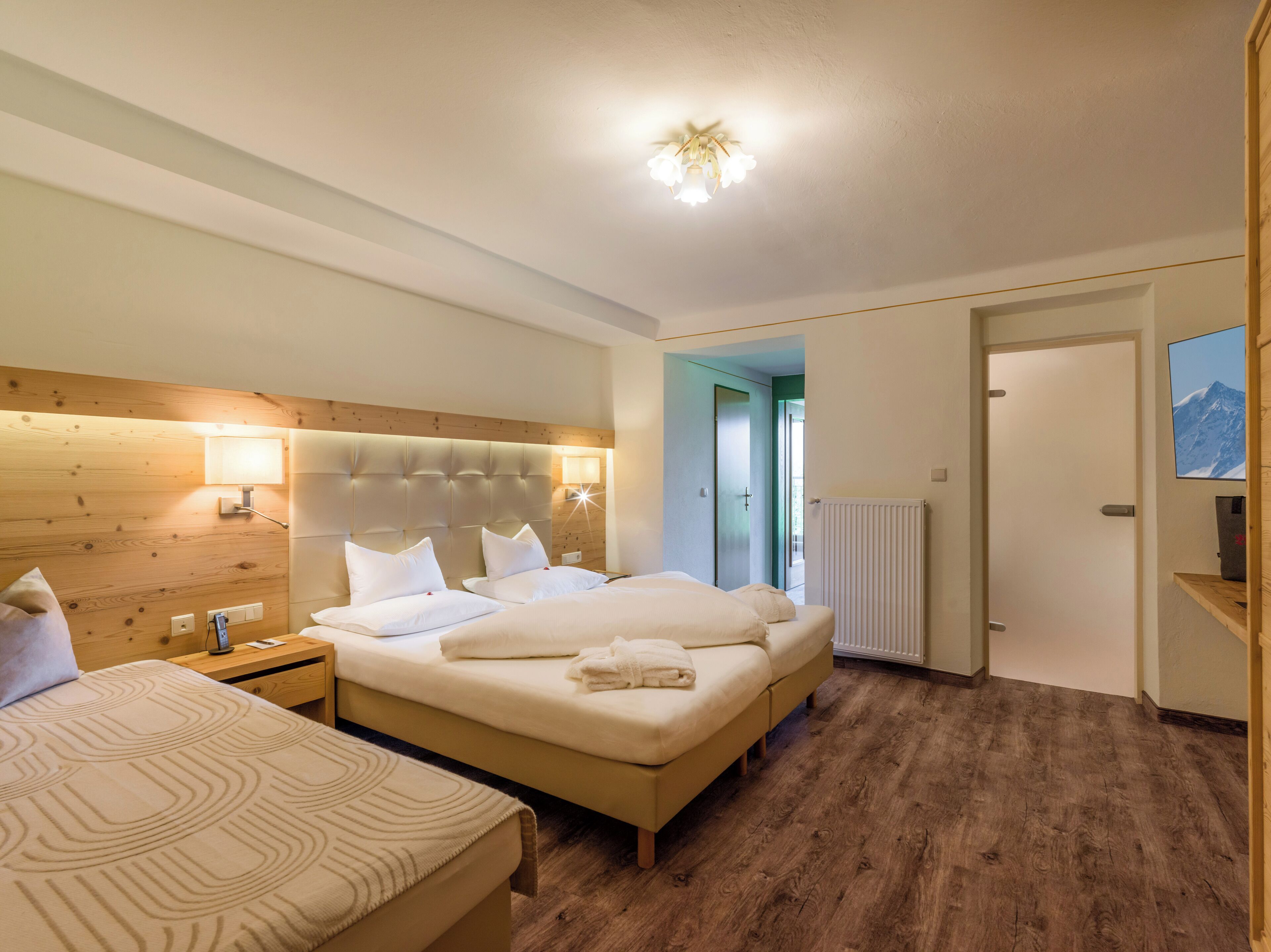 Ein Hotelzimmer mit zwei Betten, einem Holzkopfende, Nachttischlampen, einem Heizkörper und einem gerahmten Bild an der Wand.