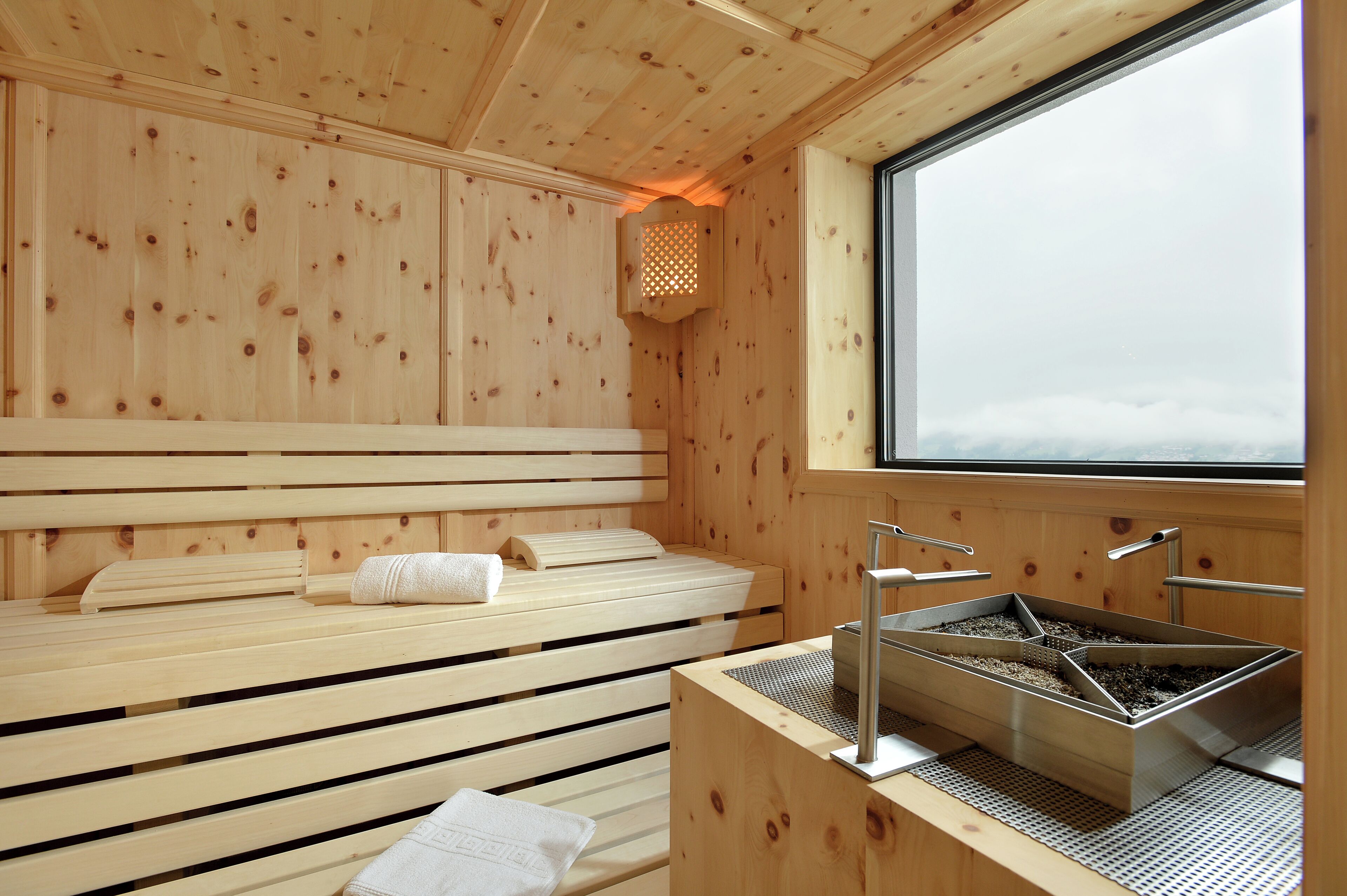Un sauna de madera con bancos, un cabezal de sauna y una ventana con vista al cielo.