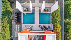 Vista aérea de un moderno espacio exterior con dos piscinas, una zona de barbacoa y un área de estar cubierta.