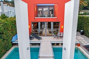 A modern building with a pool, outdoor seating, and a view of the landscape.