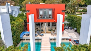 Un edificio moderno de dos pisos con piscina, mobiliario exterior y vistas al follaje circundante.