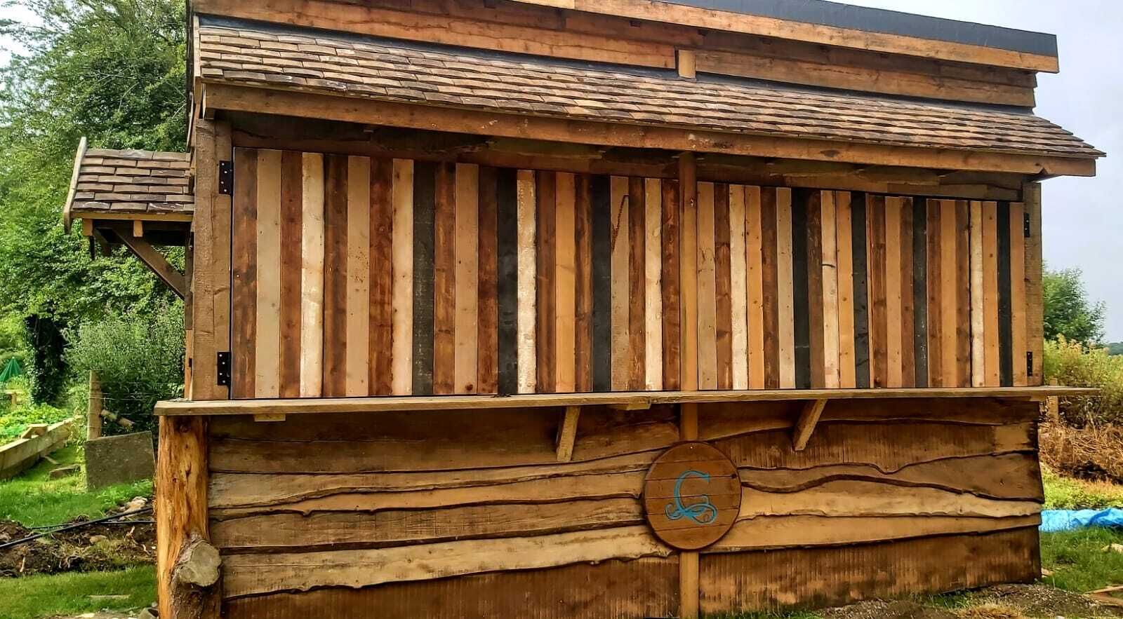 A rustic wooden structure with vertical slats, a flat roof, and a circular emblem on the front.
