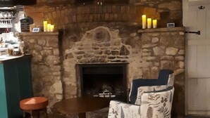 Una habitación acogedora con chimenea de piedra, una zona de bar y un espacio de descanso con una silla y un taburete estampados.