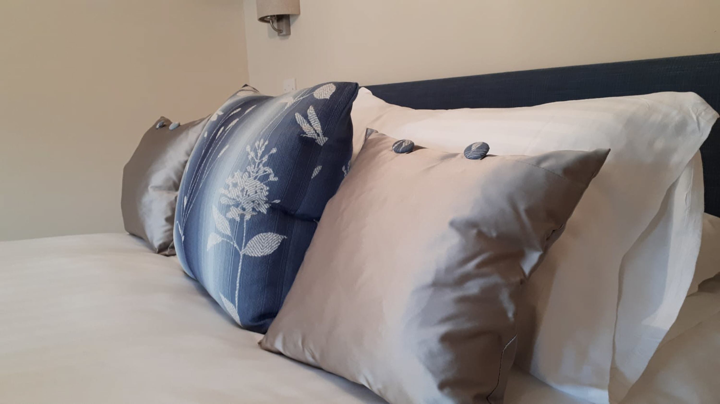 Una cama con tres almohadas, una con estampado floral y dos lisas.