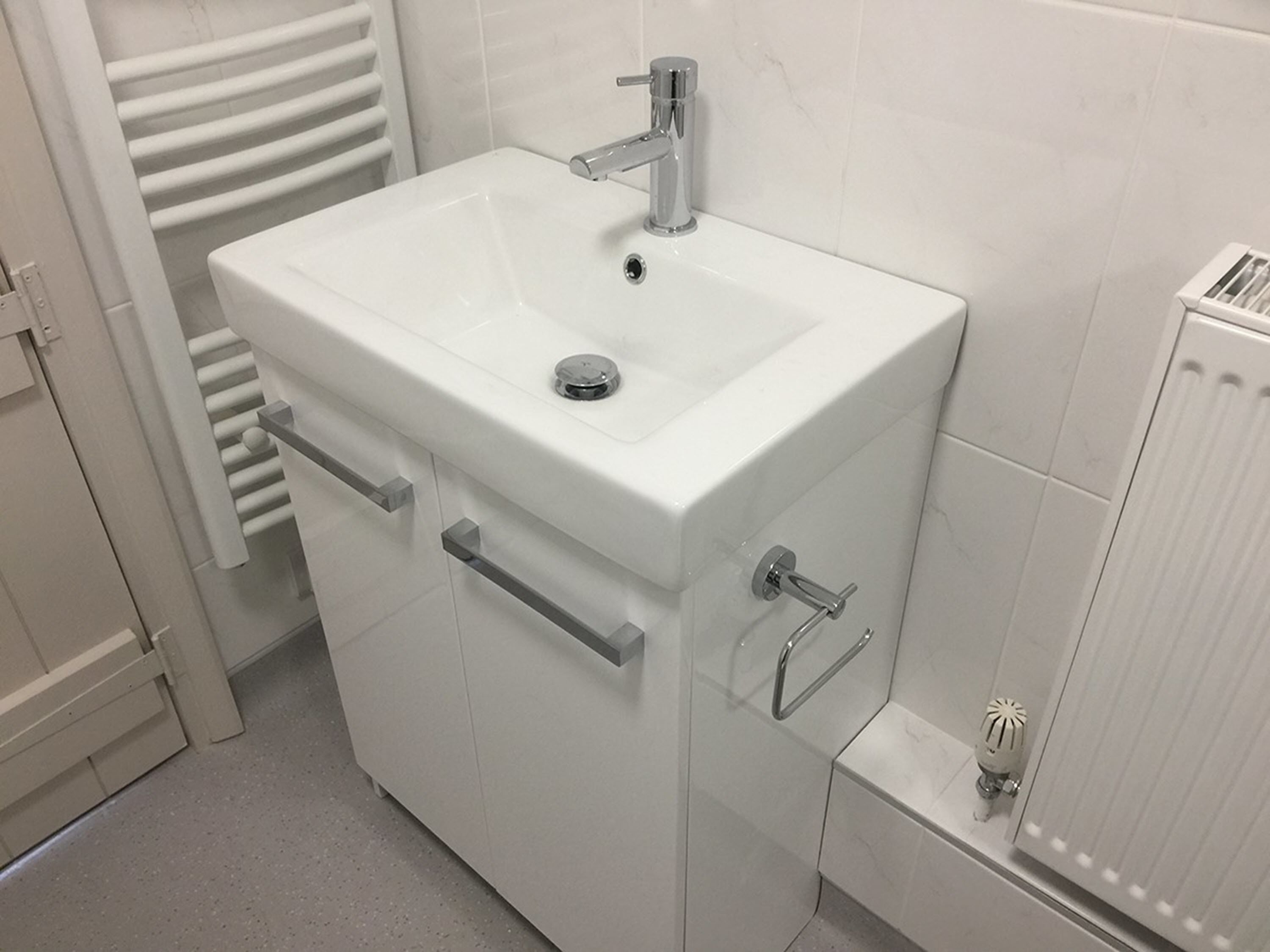 Un baño blanco con lavamanos pedestal, un perchero y un radiador.
