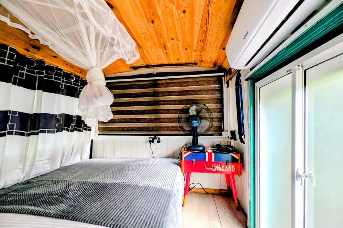A bedroom with a bed, a bedside table, a fan, and a wardrobe.