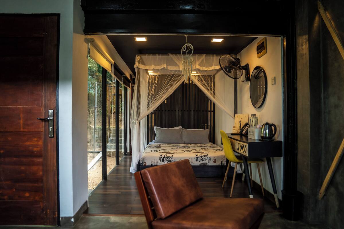 A bedroom with a canopy bed, a desk with a chair, and a view of the outdoors.
