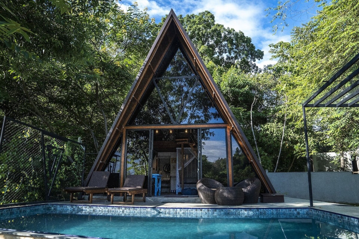 A triangular wooden structure with a pool in front.