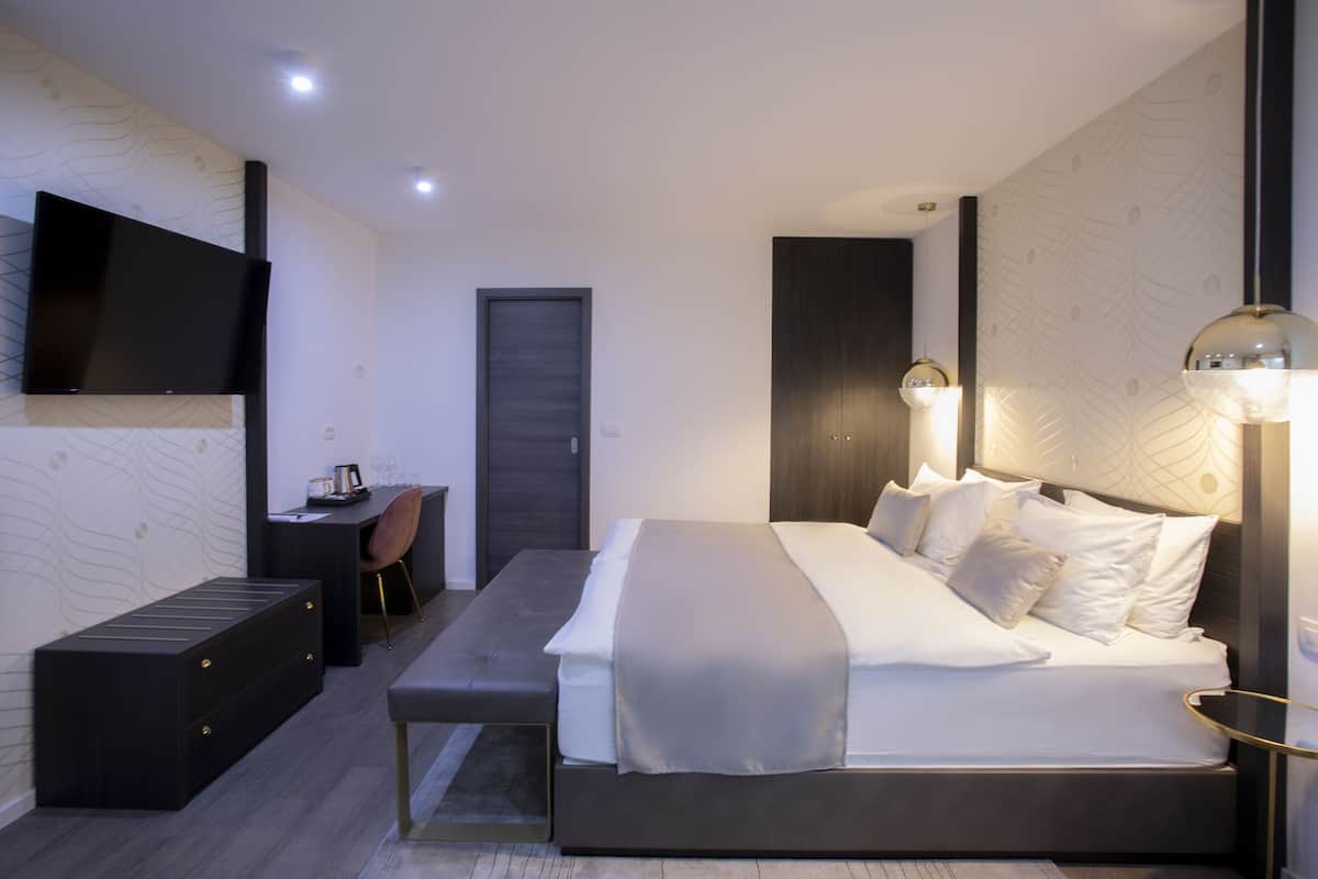 A modern bedroom with a bed, bedside table, bench, and a TV mounted on the wall.