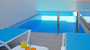 Ein Innenpool mit klarem, blauem Wasser, umgeben von blauen Liegestühlen und einem weißen Tisch mit Getränken und Obst.