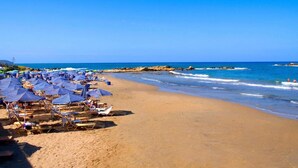 Ein Strand mit blauen Sonnenschirmen und Liegestühlen, ein sandiger Uferstreifen und das Meer.