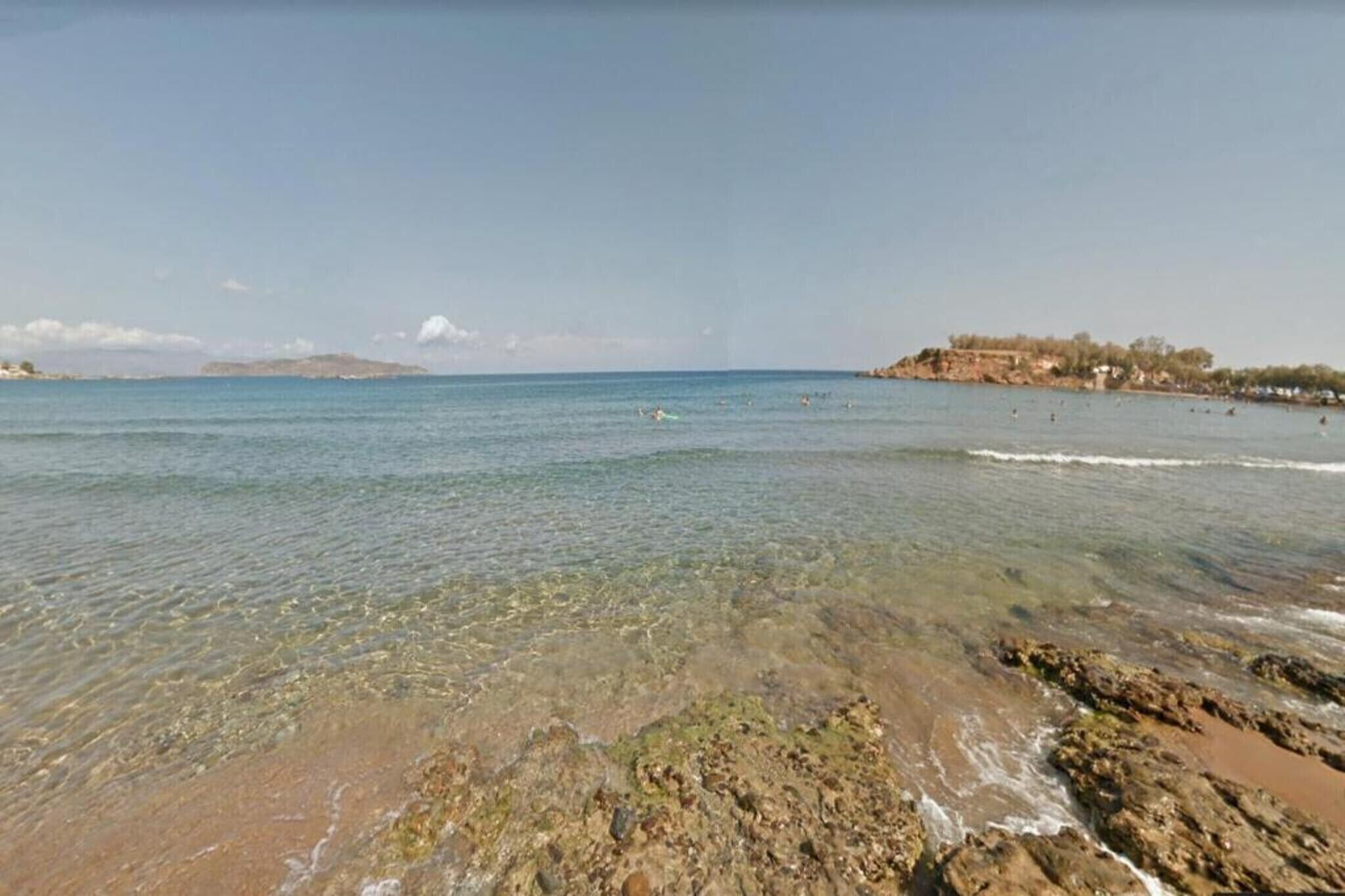 A beach with clear shallow waters, rocky shoreline, and distant hills.