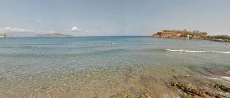 A beach with clear shallow waters, rocky shoreline, and distant hills.