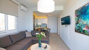 Ein modernes Wohnzimmer mit einer Couch, einem Couchtisch mit einer Vase und Blumen, einem Essbereich und einer Küche im Hintergrund.