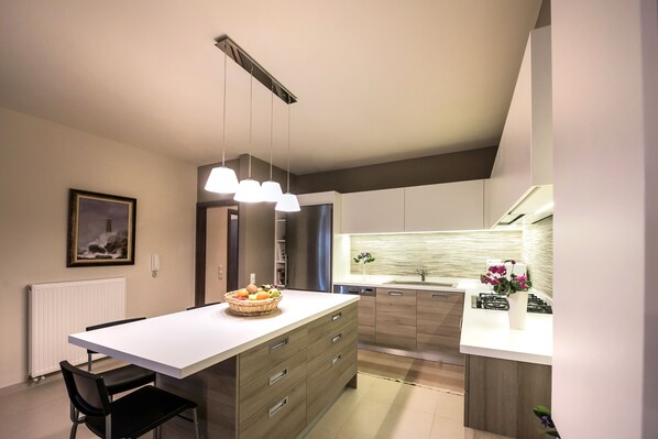Una cocina moderna con una isla central, iluminación colgante y vista al área de comedor.