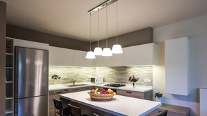 Eine moderne Küche mit Kochinsel, Edelstahlgeräten, Pendelleuchten und einer weißen Spritzschutzwand.