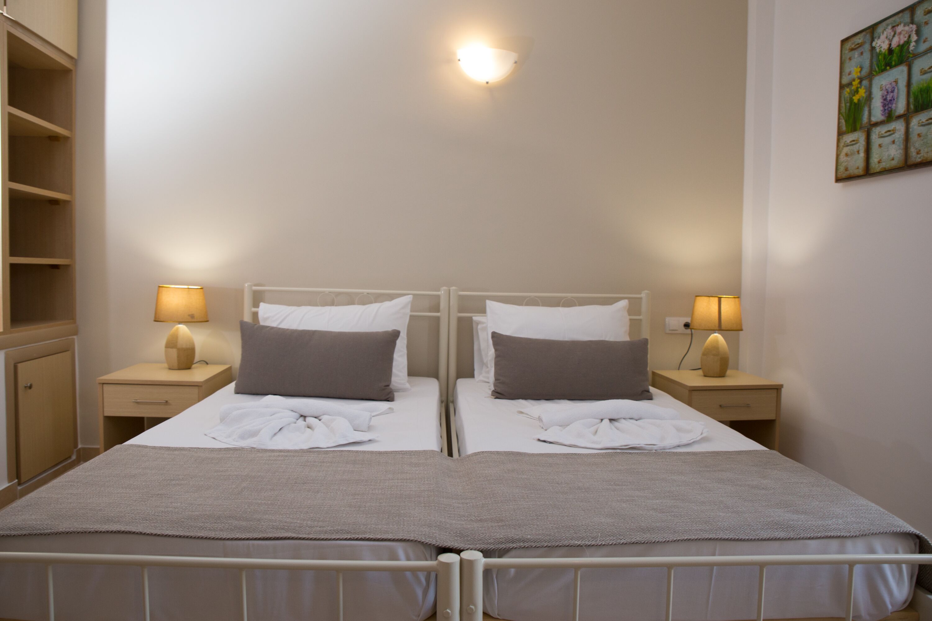 Ein Doppelbett mit weißem Kopfteil, zwei Nachttische mit Lampen, ein Holzschrank und eine Wandleuchte.