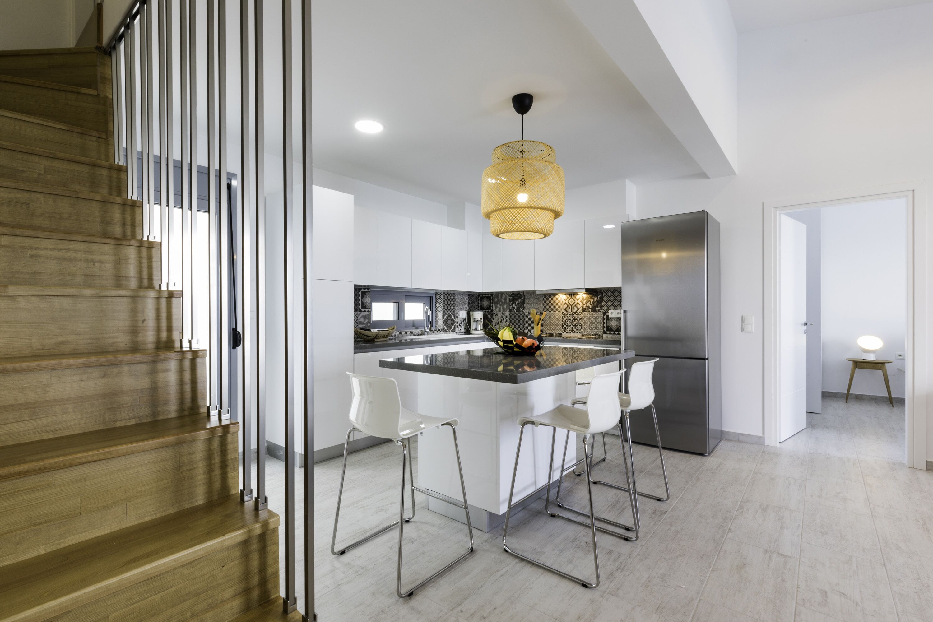 A modern kitchen with a central island, stainless steel appliances, and a wooden staircase.