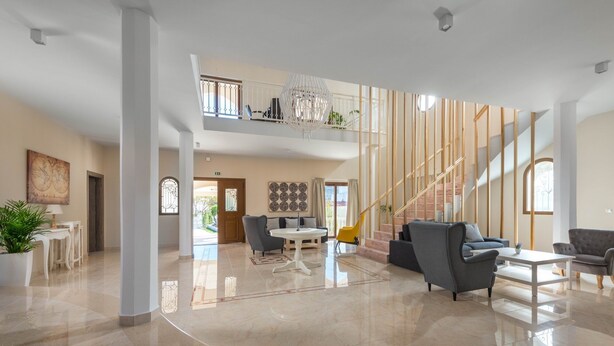 A spacious lobby with a high ceiling, a staircase, and a seating area with a round table. - Villa Evelyn with Private Pool (Αρχάγγελος)