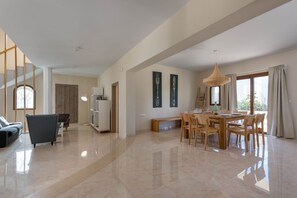 A spacious living area with a dining table, chairs, a sofa, and a bookshelf.