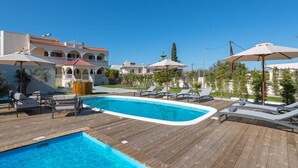 A pool area with lounge chairs and umbrellas, surrounded by buildings with balconies. - Villa Evelyn with Private Pool (Αρχάγγελος)