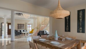 A spacious dining area with a wooden table set for four, a yellow chair, and a large woven pendant light. - Villa Evelyn with Private Pool (Αρχάγγελος)