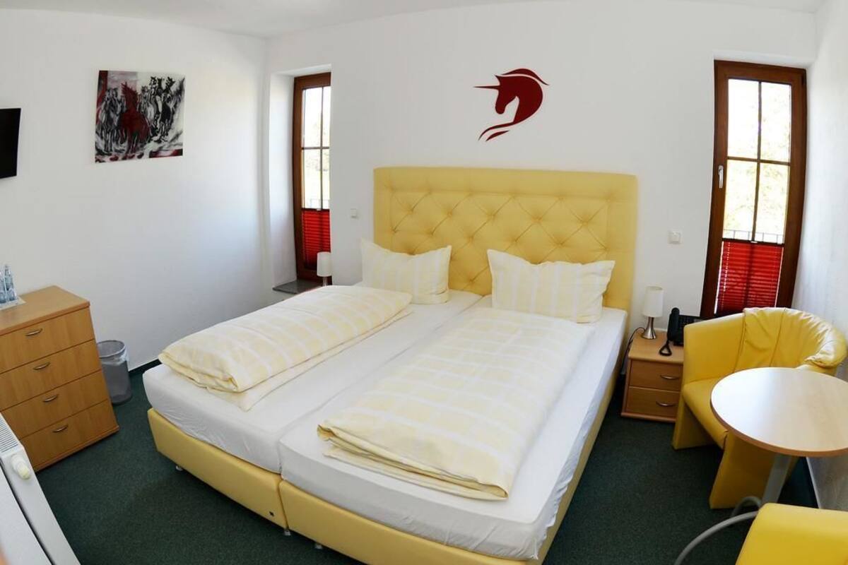 A hotel room with a double bed, a small table, a chair, a desk, and a wall-mounted artwork.
