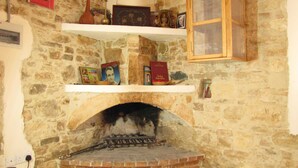 Una stanza con pareti in pietra, un camino in mattoni, scaffali con libri e oggetti decorativi, e un armadietto in legno.