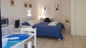 Quarto de hotel com cama, escrivaninha, cadeira, televisão, micro-ondas e uma pequena decoração de veleiro.
