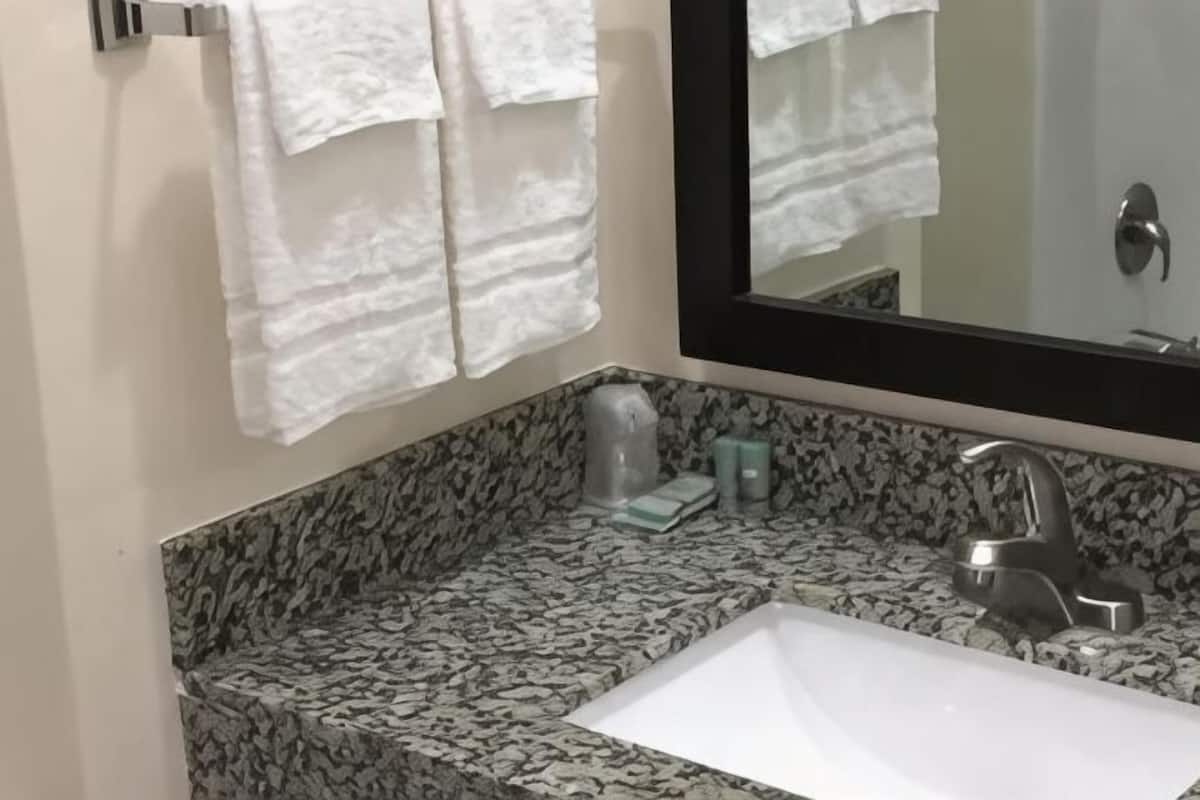 A bathroom with a granite countertop, a white sink, a mirror, and white towels hanging on a rack.