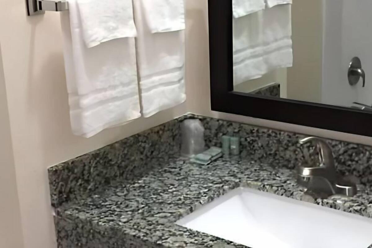 A bathroom with a granite countertop, a white sink, a mirror, and white towels hanging on a rack.